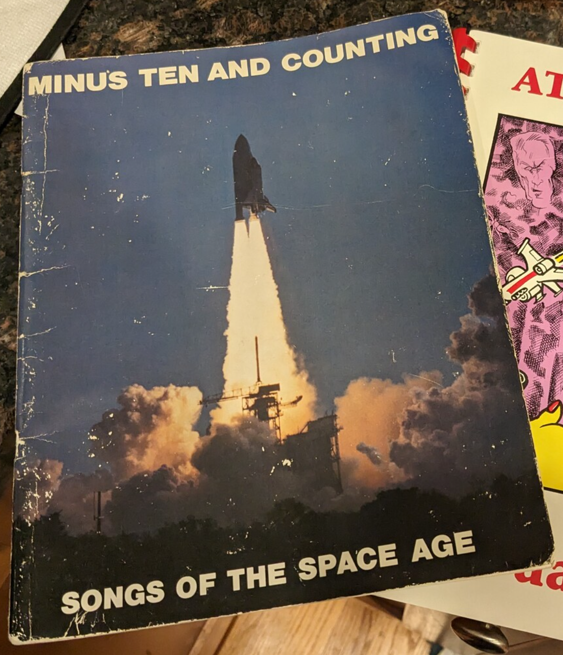 the Minus Ten and Counting: Songs of the Space Age songbook. It is
significantly boxed at the edges and bears a photograph of the Space Shuttle
taking off, sans megagantry.